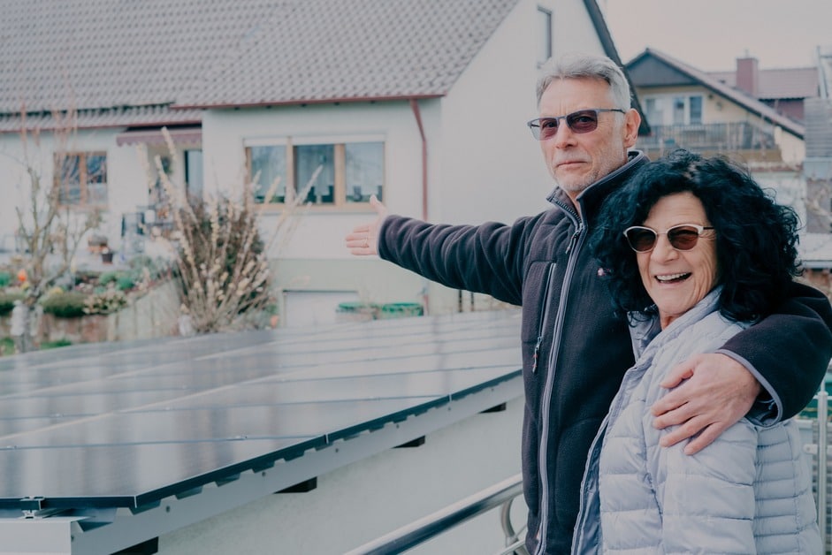 Ein Kundenpaar steht draußen neben einer Photovoltaikanlage und zeigt auf die installierten Solarmodule