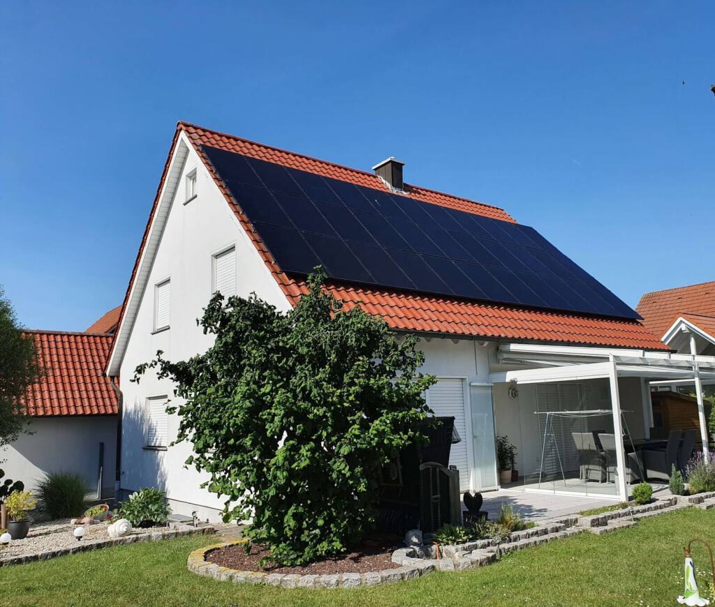 Ein Einfamilienhaus mit rotem Ziegeldach, auf dessen Dachfläche eine großflächige Photovoltaikanlage installiert ist