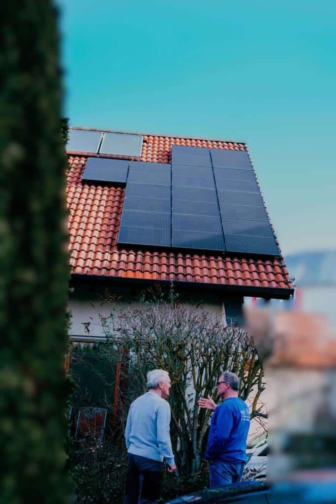Zwei Personen stehen im Garten vor einem Reihenhaus und sprechen miteinander. Auf dem Dach sind Photovoltaikmodule montiert.
